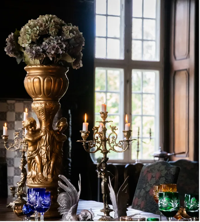 Forgyldt vase med hortensia, kandelabre og levende lys ved vinduet i en af Visborggaard Slots historiske stuer